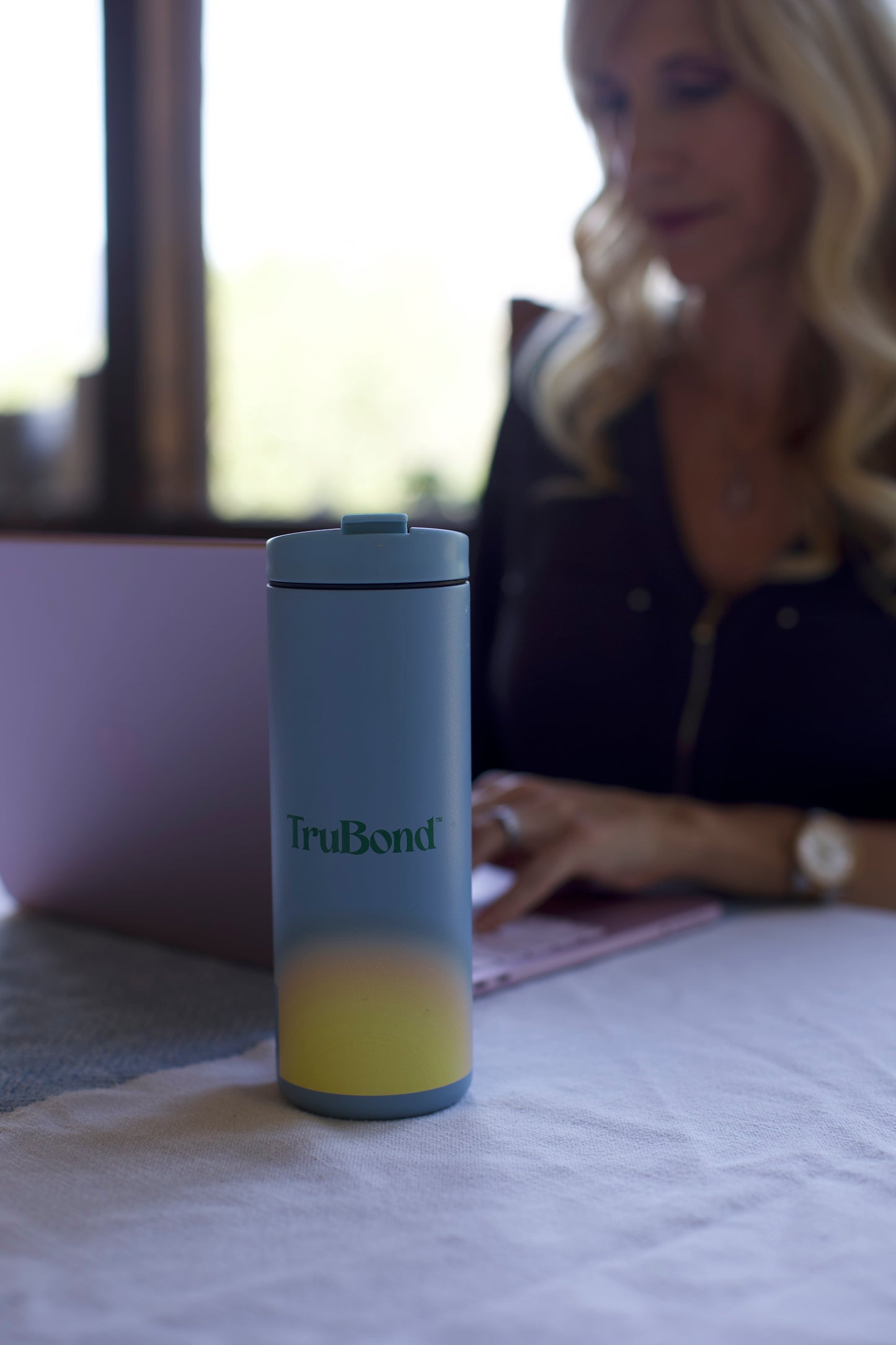 TruBond x Miir Flip traveler tumbler on a table with a blurred background of a person using a laptop.