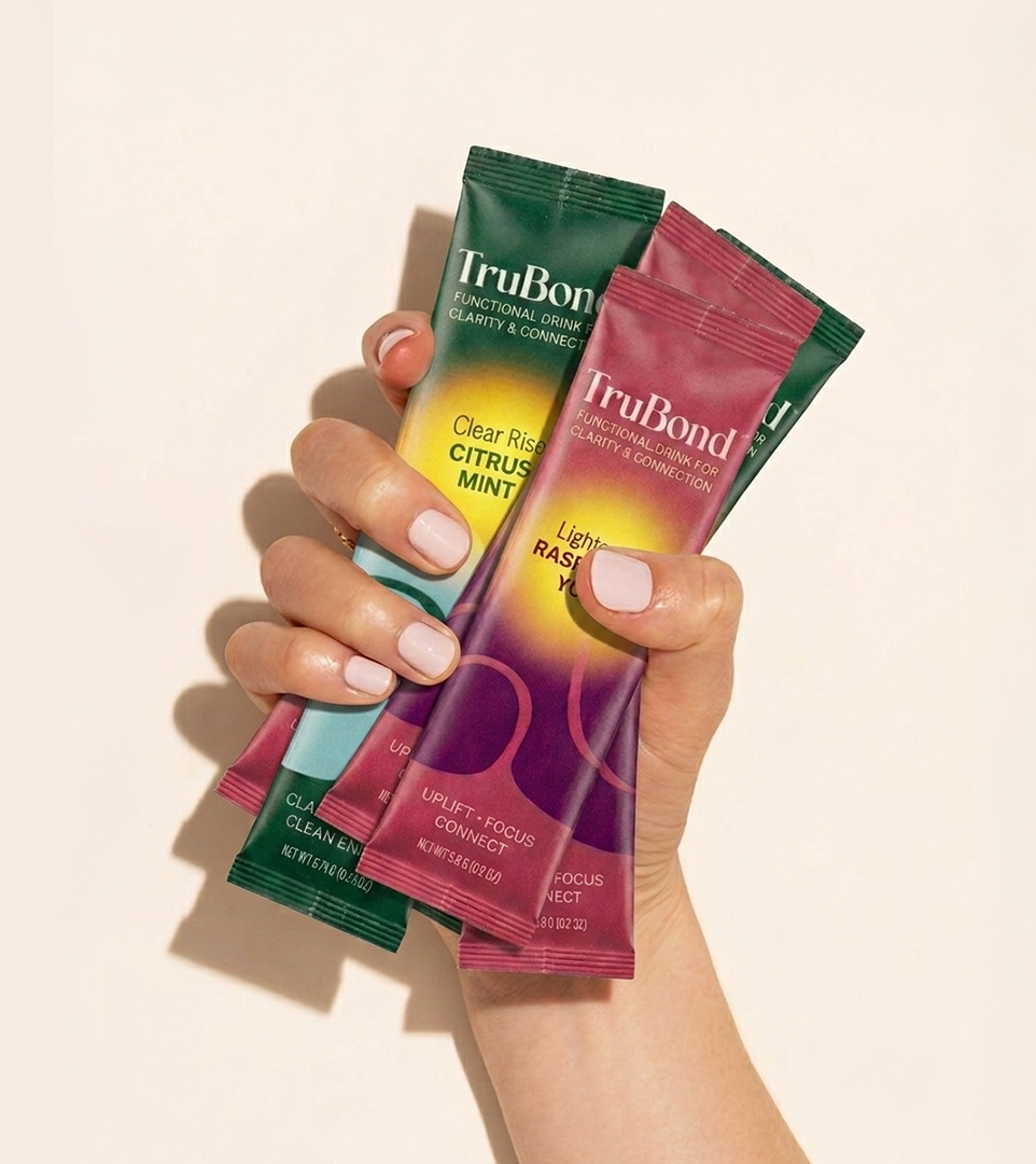 Hand holding four TruBond stick packs against a beige background